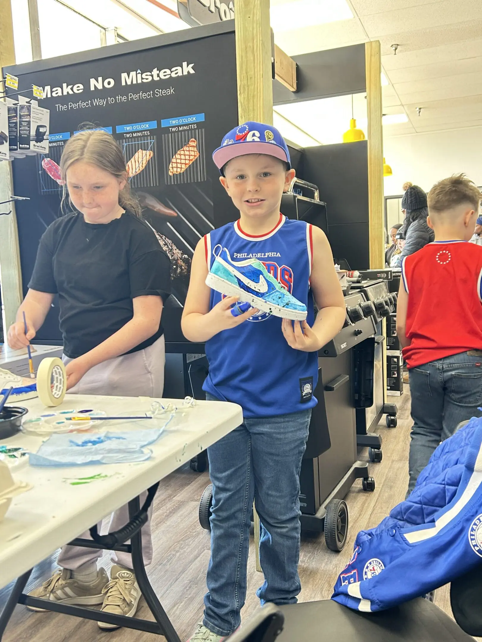 Boy holding a colorful sneaker at a shoe customization event.