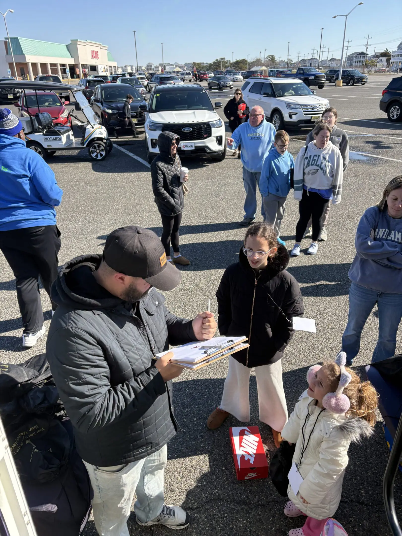 People gathered outside in winter clothing, some interacting and taking notes.
